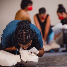 Individuals in a CPR training class practicing chest compressions and breaths on CPR manikins